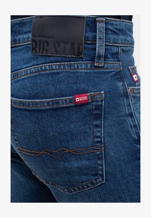 Sinine denim teksad, millel on suur must nahast silt, millel on kiri "BIG STAR" ja punane silt tagakotil valge tähe detailiga.