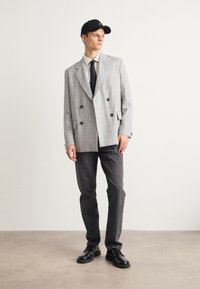 Gray checkered double-breasted blazer, black tie, dark denim jeans, black shoes, and black cap. Smooth fabric with large buttons and sharp lapels.