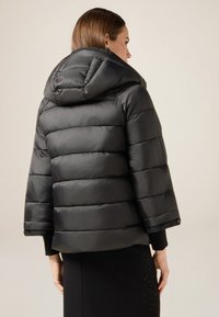 Czarna puchowa kurtka z kapturem, z pikowanym wzorem i krótkimi rękawami. Gładka faktura z lekko błyszczącym wykończeniem.