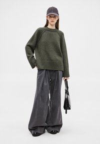 Ülerahvastatud oliivroheline kampsun soonikkoes äärega, mida kantakse laia halli pükste ja mustade platvormjalanõudega. Tumeda halli palsameeriga müts ja käekott täiendavad välimust.