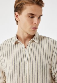 Cremetigerne Hemd aus strukturiertem Stoff mit marineblauen Streifen, Knopfleiste und klassischem Kragen.