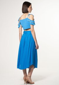 Top corto blu scollato con maniche a volant, abbinato a una gonna blu plissettata e sandali beige con tacco alto.
