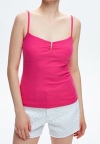 Dopasowany różowy top na ramiączkach z prążkowanej tkaniny, z cienkimi ramiączkami i detalem w kształcie dziurki na środku, zestawiony z białymi szortami z wyciętymi elementami i falbanowanym dołem.