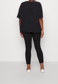 Svart löst sittande topp med korta ärmar, med en texturerad design på ärmarna, i kombination med smala svarta leggings och vita platta skor.