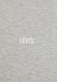 Šedá bavlněná tkanina s hladkou texturou, na které je uprostřed bílé vyšívané logo "LEVI'S". Jednoduchý a minimalistický design.