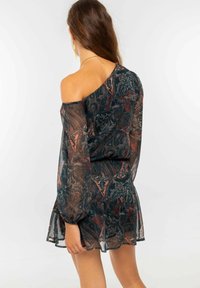 Vestido off-shoulder de tela oscura con un intrincado estampado de paisley en rojo y verde azulado. Mangas largas y transparentes con un dobladillo con volantes.