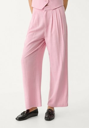 Personne portant un pantalon rose ample et taille haute avec des plis, assorti à des mocassins noirs à glands.