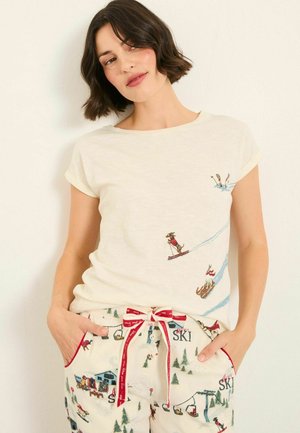 Cotton t-shirt in light cream with short sleeves, featuring playful ski-themed embroidery. Paired with patterned drawstring pants.