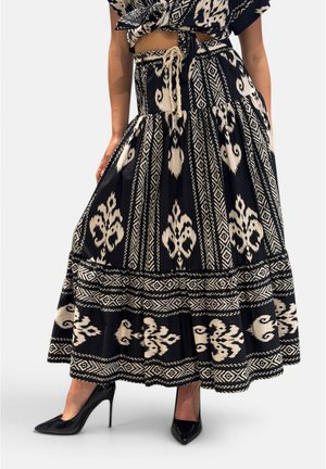 Gonna lunga (maxi) nera e beige con fantasia e orlo ampio, abbinata a un top corto annodato e scarpe nere con tacco alto e punta appuntita.