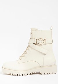 Bota de combate de cuero blanco con puntera redonda, cordones delanteros, detalle de hebilla lateral con un logo circular y suela robusta con tacos pronunciados.