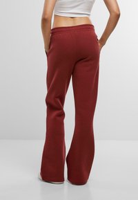 Sarkani platiem sporta bikses ar elastīgu jostasvietu, sānu kabatām un mīkstu tekstūru. Dizains ietver brīvu piegriezumu un apavu garuma kājas.