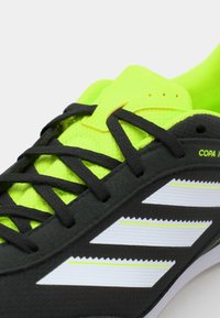 Scarpa da calcio nera con accenti verde brillante, con una tomaia testurizzata, lacci neri e tre strisce bianche diagonali ai lati.