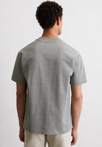 Szara koszulka z krótkim rękawem, wykonana z bawełny, z okrągłym dekoltem i gładką fakturą. Z tyłu znajdują się minimalne detale przeszycia.