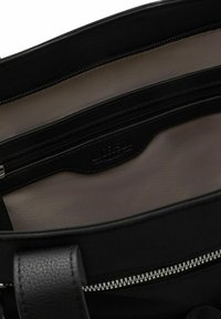 Die Innenseite der schwarzen synthetischen Handtasche verfügt über ein glattes, hellbeiges Futter, mehrere Reißverschlussfächer und ein markantes, eingeprägtes Markenlabel.