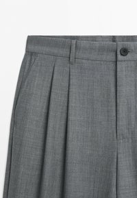 Gray pleated trousers with belt loops, side pocket, and button closure at the waistband.