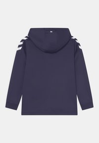 Marinblå munkjacka med lång ärm, som har vita ränder på axlarna, en slät yta och justerbar dragsko i huvan.