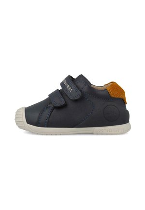 Zapato infantil azul marino con doble tiras de velcro, suela blanca y parche de ante marrón en el talón, vista lateral sobre fondo blanco.