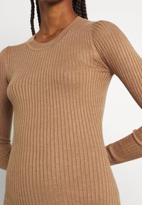 Pull en maille côtelée marron avec manches longues, dotée d'un col rond et d'un tissu texturé qui s'ajuste étroitement au corps.