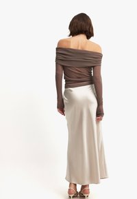 Bruine off-shoulder gebreide top met lange mouwen, gecombineerd met een lange, lichtbeige satijnen rok. Soepele textuur, eenvoudig ontwerp en neutrale kleuren.