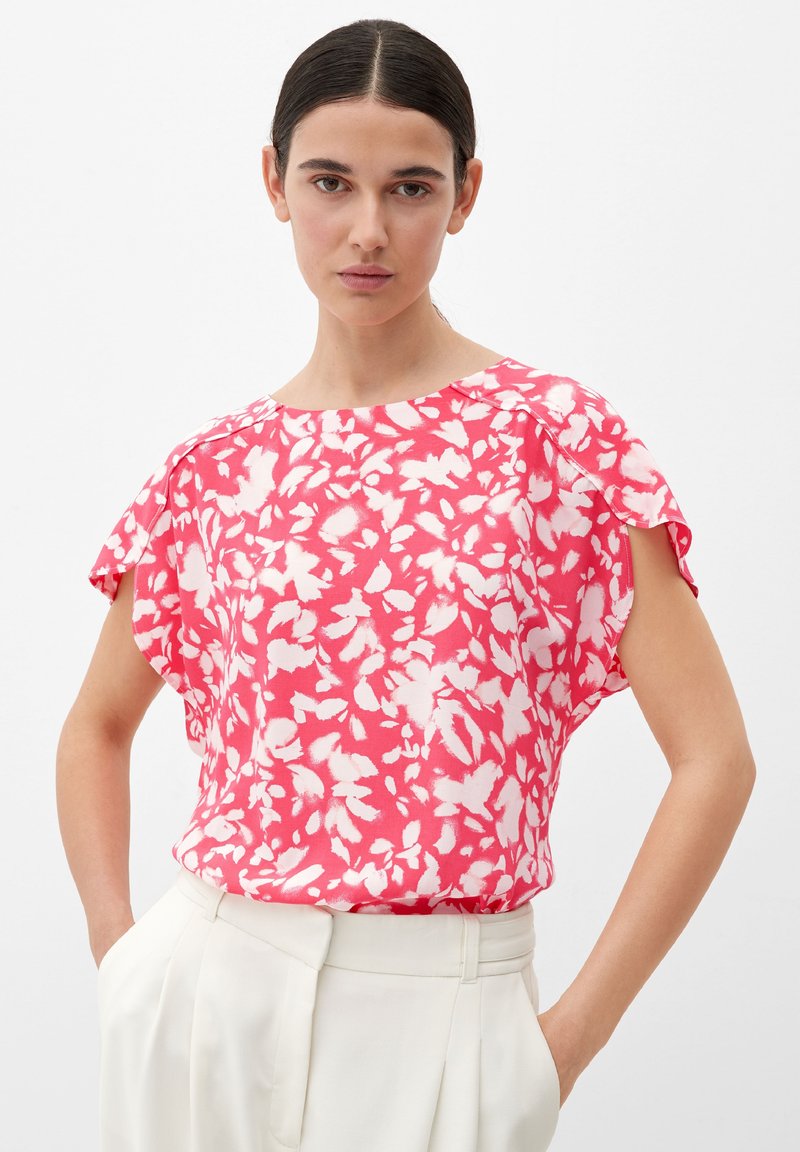 Rosa und weiße Bluse mit kurzen Ärmeln, lockerer Passform und rundem Ausschnitt, kombiniert mit hochtaillierten weißen Hosen. Glatte Stofftextur.