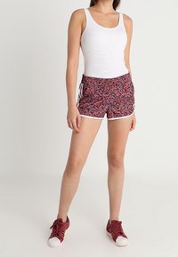 Bílá tílko spárované s červenými a navy vzorovanými šortkami s bílým lemem a šňůrkou. Nosit s vínovými teniskami.