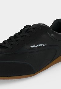 Μαύρο sneaker Karl Lagerfeld με κλείσιμο με κορδόνια και καφέ λαστιχένια σόλα, που δείχνει το λογότυπο στο πλάι και υφή λείας δερμάτινης επιφάνειας.