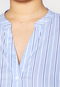 Lichtblauw button-up shirt met verticale witte en blauwe strepen, V-hals en zachte stofstructuur. Heeft een eenvoudig kraagontwerp.