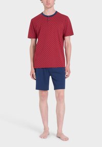 Maglietta rossa a maniche corte con pois bianchi, colletto blu navy e dettaglio dei bottoni, abbinata a pantaloni corti blu navy. Tessuto di cotone leggero.