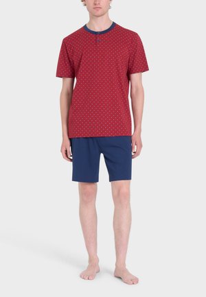 Maglietta rossa a maniche corte con pois bianchi, colletto blu navy e dettaglio dei bottoni, abbinata a pantaloni corti blu navy. Tessuto di cotone leggero.