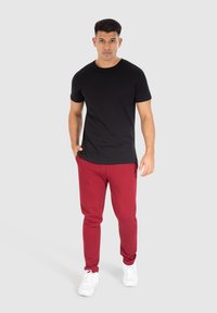 Zwarte t-shirt met korte mouwen gecombineerd met rode joggingbroek. Witte sneakers maken de outfit compleet. De stof lijkt soepel en casual.