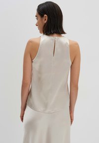 Top senza maniche in seta di colore beige chiaro, con dettaglio a chiave sulla schiena e una leggera texture, progettato per un fit rilassato.