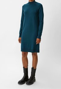 Abito lavorato a maglia teal con collo alto e maniche lunghe, caratterizzato da un orlo a coste. Abbinato a stivali neri alla caviglia con suola spessa.