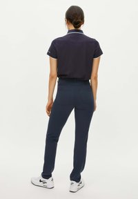 Marineblauwe polo met witte afwerking, gecombineerd met marineblauwe slim-fit broek. Witte sneakers met zwarte accenten. Weergave van achteraf.