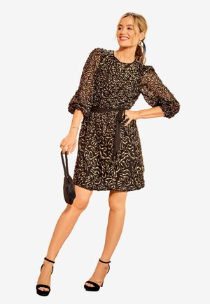 Musta mekko, jossa on läpinäkyvät puffihihat ja tiukka bodice, koristeltu kultaisella kieppu kuvioilla, joka on vyötetty mustalla vyöllä vyötäröltä.