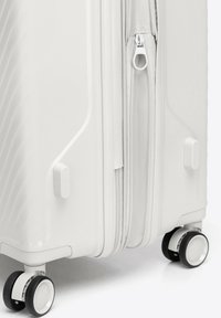 White hard-shell suitcase with a textured surface. Features a zip closure, smooth wheels, and sturdy plastic accents for support.