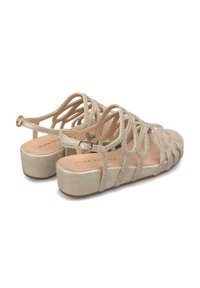 Sandali a strappo beige con suola piatta, decorati con dettagli scintillanti e una fascia con fibbia, caratterizzati da una texture liscia e un design aperto.
