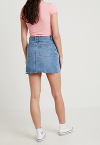 Jeanskjol med fransad fåll, i medellängd och två bakfickor. Kombinerad med vita canvas-sneakers och en rosa ribbad topp.