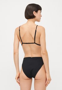 Black two-piece swimsuit featuring a ribbed texture, adjustable straps, and medium-height bikini bottom. Minimalist design with golden hardware accents.
