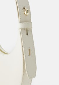 Cream leather handbag with a rounded shape, featuring a smooth texture, adjustable strap, and gold-tone hardware accents.