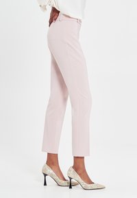 Hellrosa maßgeschneiderte Hose mit schlanker Passform, verkürzter Länge und glatter Textur, kombiniert mit High Heels im Schlangenprint-Design.