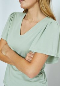 Halenka s krátkým rukávem ve tvaru V v jemné mátově zelené látce, s nabíranými rukávy, přiléhavým střihem a jemným prošíváním.