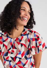 Korte mouwen blouse van lichtgewicht stof met een geometrisch patroon van rode, blauwe, zwarte en beige vormen. Geraffineerde halslijn.