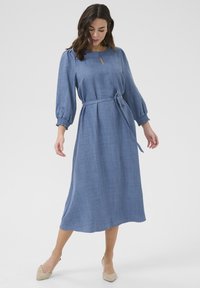 Robe midi bleu à manches longues avec un tissu texturé. Caractéristiques d'un décolleté en forme de clé et d'un lien en tissu à la taille. Silhouette douce et fluide.