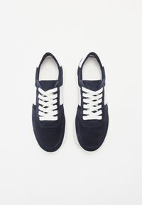 Baskets en daim bleu marine avec lacets blancs, présentant un accent blanc sur le côté, un bout arrondi et une semelle rembourrée. Conçues pour un usage décontracté.