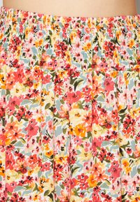 Saia floral com um cós franzido, apresentando uma estampa vibrante de flores vermelhas, rosas, laranjas e amarelas sobre um fundo azul claro.