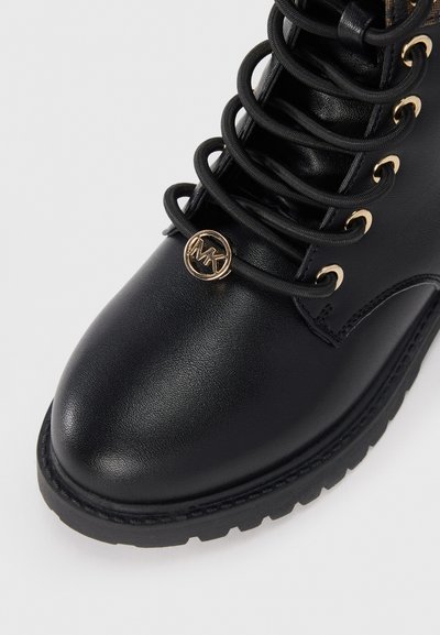 Botte de cheville en cuir noir avec bout rond, surface texturée, accent logo doré et lacets noirs passant par des œillets dorés.