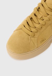 Zapatilla de ante amarilla con superficie texturizada, puntera redondeada y cordones prominentes. Cuenta con una suela de goma con patrón y detalle del logo.