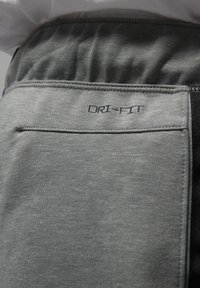 Zbliżenie na szare sportowe spodnie z elastycznym paskiem w talii i tylną kieszenią oznaczoną napisem "DRI-FIT."