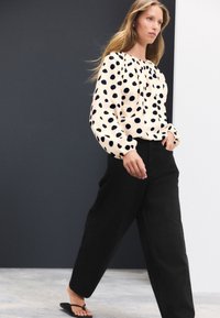 Krämfärgad blus med marinblå prickar, rynkad halsringning och långa ärmar. Svarta vida byxor och svarta flip-flops kompletterar outfiten.