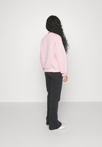 Lys rosa sweatshirt med lange ermer, løs passform, ribbede ermer og kant, kombinert med mørke svingende jeans og flerfargede mønstrede sko.